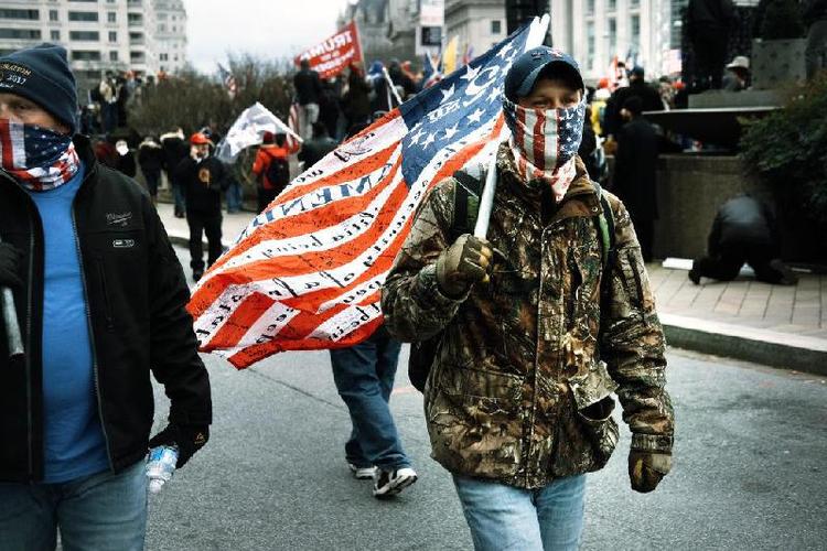 Apoiador de Donald Trump com jaqueta clamufada carrega bandeira dos EUA e veste mscara com bandeira dos EUA