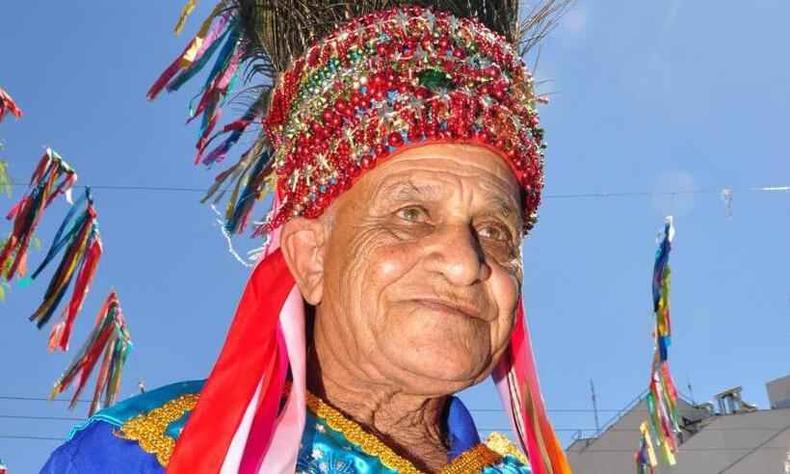 Mestre Zanza com 'capacete' de fitas coloridas e penas de pavo