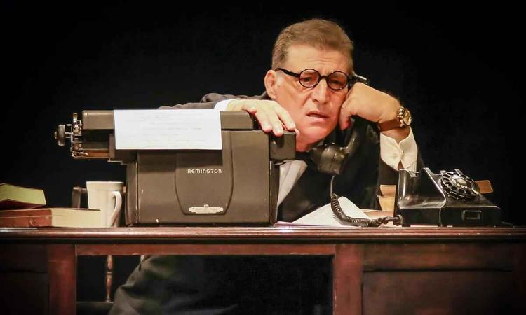 Ator Giuseppe Oristanio usa culos e est caracterizado como Guimares Rosa, sentado  mesa de trabalho, na pea Pormenor de ausncia
