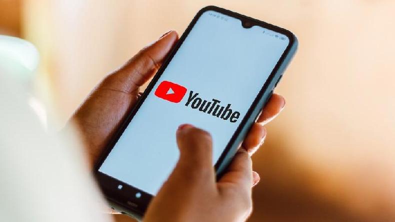 Mo de mulher segurando um smartphone, no qual o logotipo do YouTube  exibido na tela