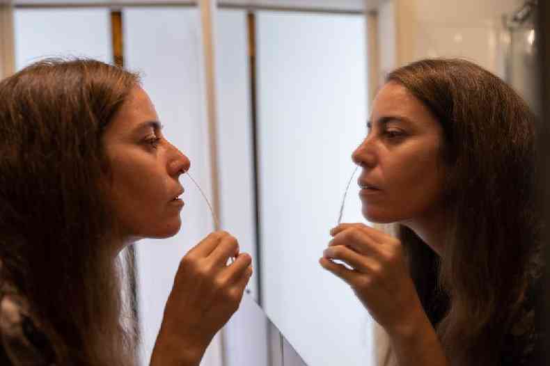 Mulher colhendo amostra do nariz na frente do espelho para fazer teste rápido de covid-19