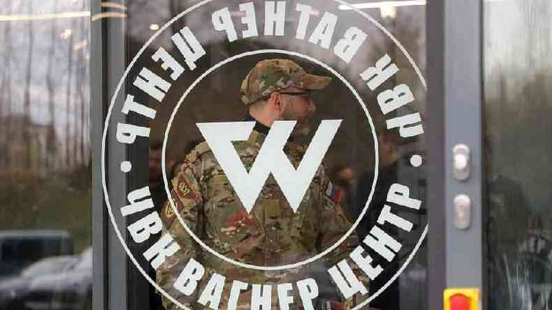 Homem com uniforme camuflado atrs de porta com smbolo do grupo Wagner