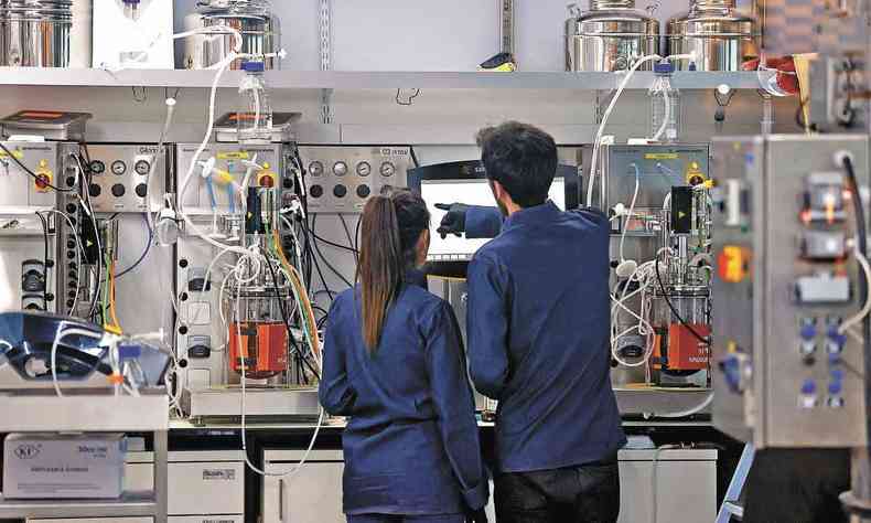 Uma jovem e um jovem de costas e uniforme azul trabalham em equipamento eletrônico