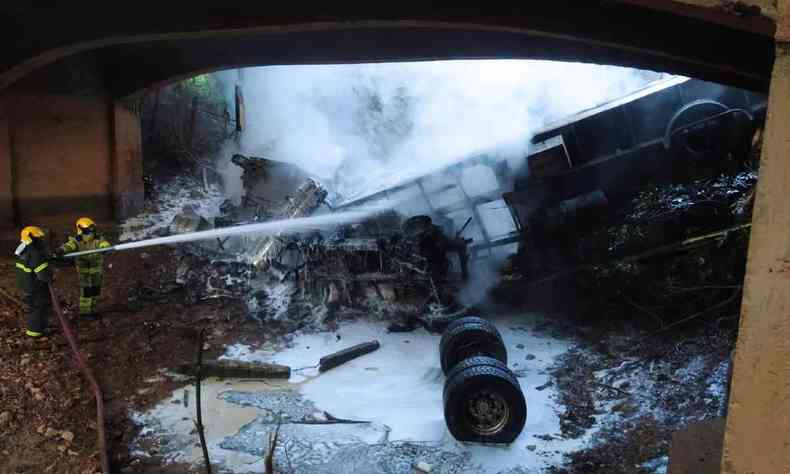 Na foto, carreta tombada debaixo de uma ponte, enquanto bombeiros controlam as chamas