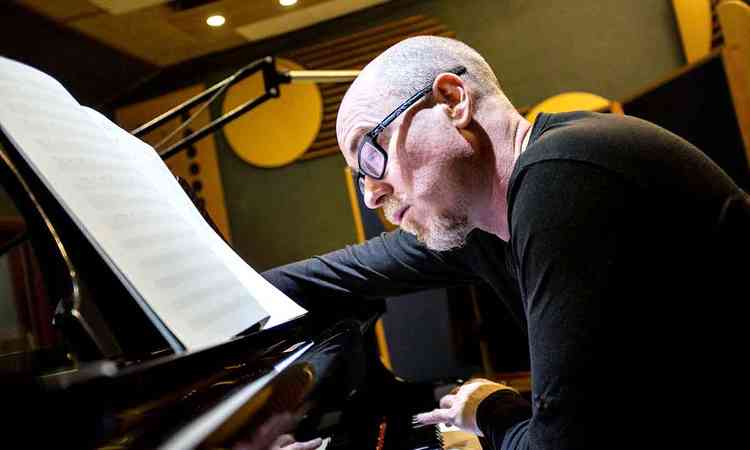 Vestido de preto e usando culos, Vladimir Safatle l partitura e toca piano
