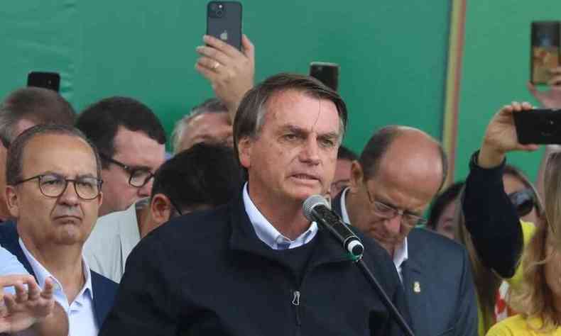 Presidente Jair Bolsonaro fala em um microfone ao lado de apoiadores