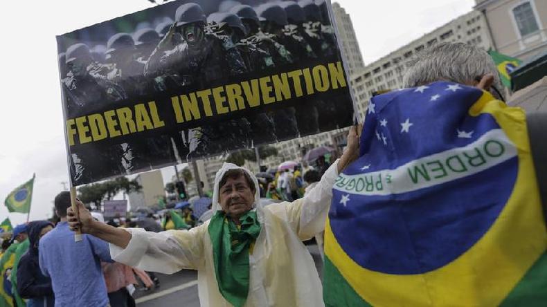 Senhora na rua levanta cartaz com foto de militares e pedido em ingls por 'Federal intervention'