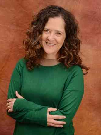Usando blusa verde e de braos cruzados, a escritora Carla Madeira olha para a cmera e sorri 