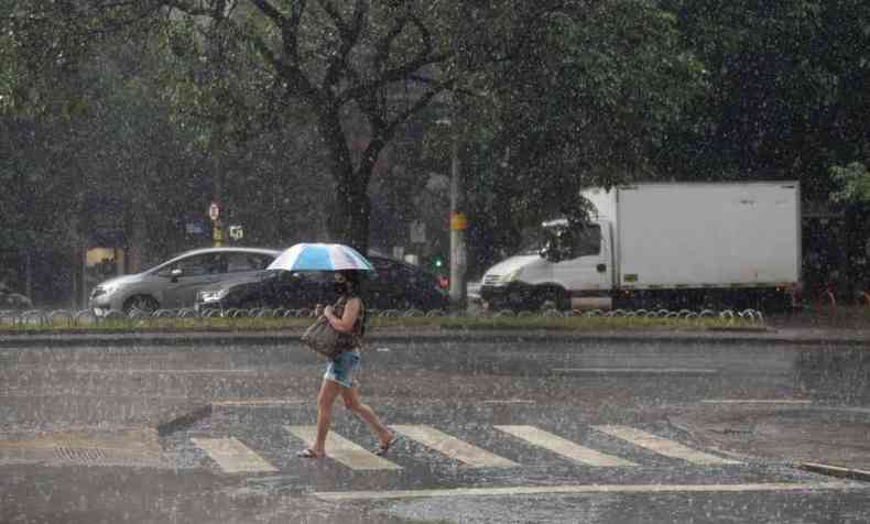 Mulher com guarda-chuvas atravessa a rua em meio a chuva em BH