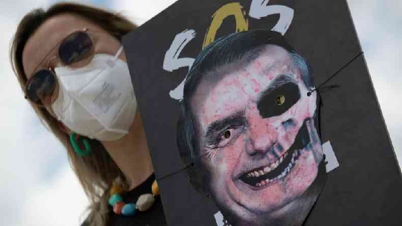 Mulher de mscara segura cartaz em que foto de Bolsonaro foi transformada em figura assustadora