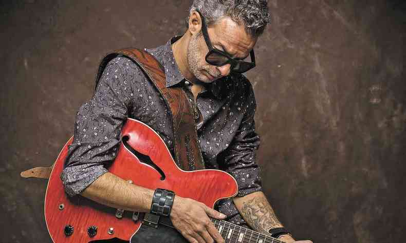 De óculos escuros e cabeça baixa, Luca Giordano segura sua guitarra com a mão direita