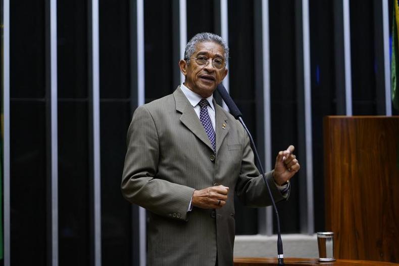 Retrato do deputado federal Vicentinho (PT-SP) na tribuna do Plenrio da Cmara dos Deputados. Ele  um homem negro. Veste camisa social branca e prpura com um terno cinza esverdeado.