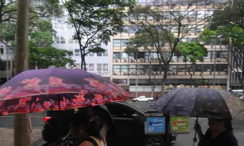 Imagem de pessoas caminhando na rua com guarda-chuvas e sombrinhas