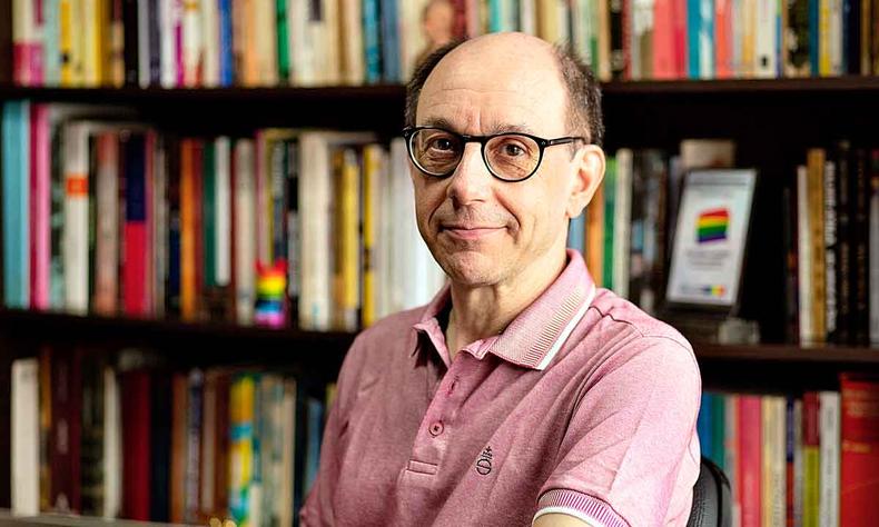 O escritor Luiz Morando olha para a cmera. Atrs dele h estante cheia de livros