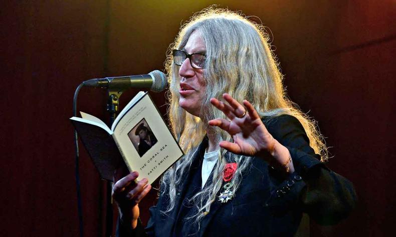 Em frente ao microfone, a cantora e escritora Patti Smith declama, segurando o livro The coral sea