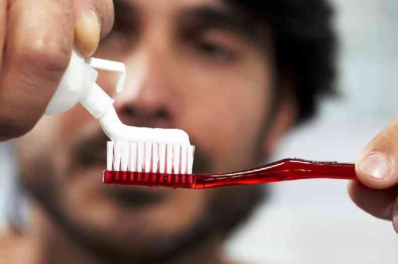 Homem passando pasta de dente em escova comum