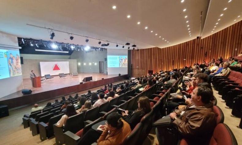 Auditrio com vrias pessoas sentadas em frente a uma tela com a bandeira do estado de Minas Gerais projetada