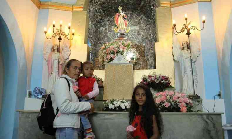 Mulher com criana no colo e uma menina diante do altar da capela