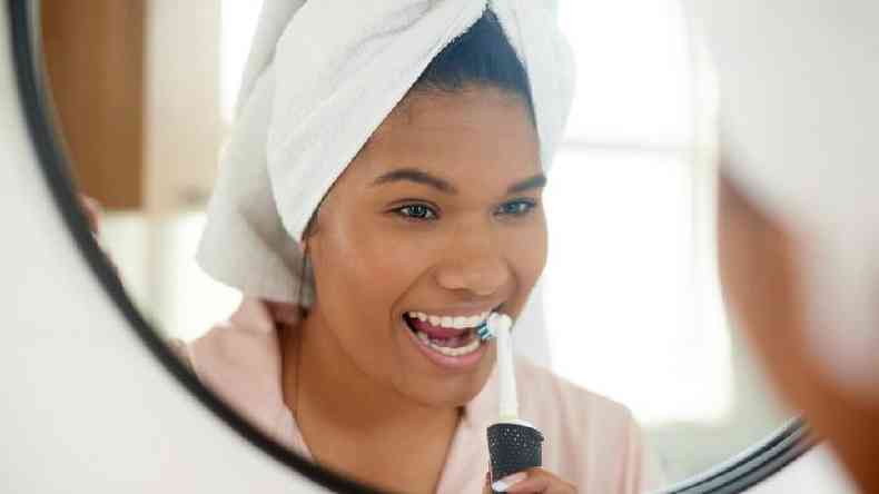 Mulher escovando o dente com escova elétrica em frente ao espelho