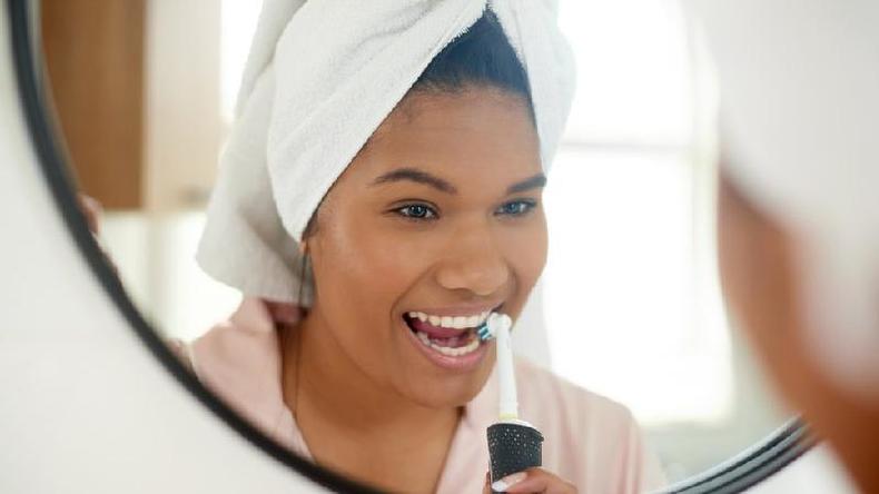 Mulher escovando o dente com escova eltrica em frente ao espelho