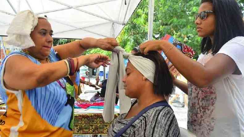 Vendedoras ajudando mulher a vestir turbante