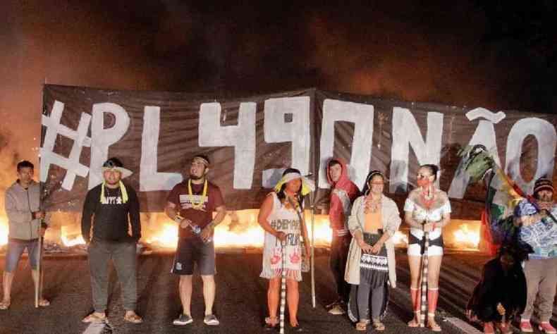 Indgenas Guarani com faixa escrito 'PL490 no' e pneus queimando ao fundo em protesto na rodovia Bandeirantes, So Paulo