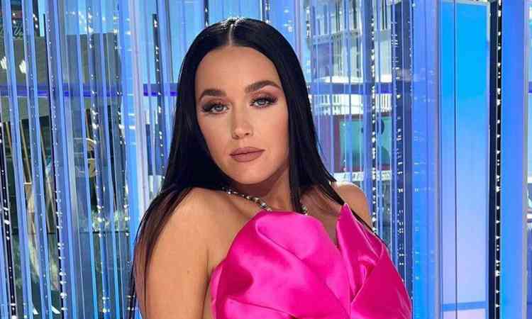 Katy Perry veste uma roupa rosa e est em um cenrio com fundo azul