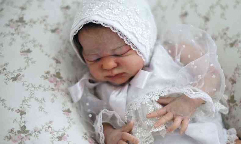Boneco de beb de touca e roupa branca tem os olhos fechados, como um recm-nascido de verdade