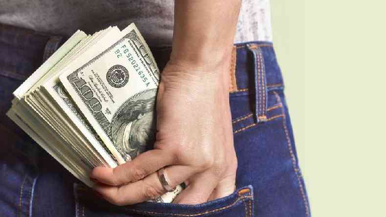 Pessoa coloca notas de dólar no bolso de uma calça