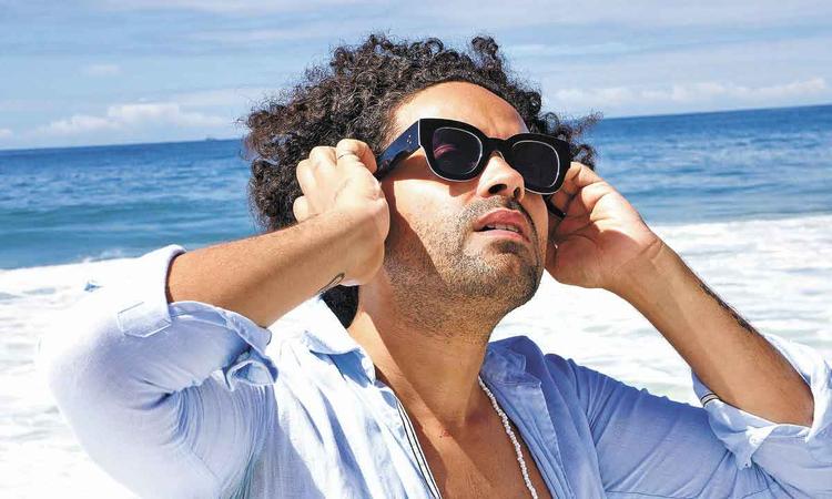 De culos escuros, Csar Lacerda inclina o rosto na direo do sol, na praia
