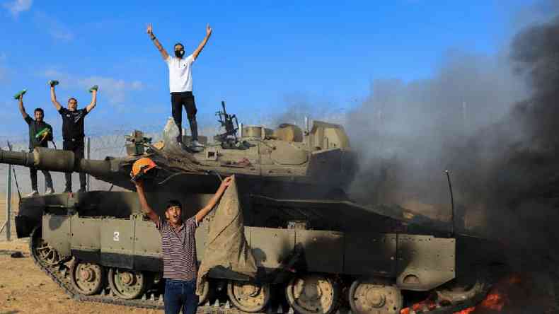 Palestinos comemoram enquanto um veculo militar israelense pega fogo depois de ter sido atingido por homens armados que se infiltraram em reas do sul de Israel, no lado israelense da fronteira 