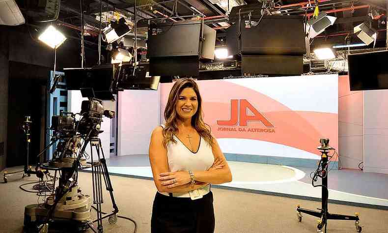 A apresentadora Carolina Saraiva sorri, de braos cruzados, tendo ao fundo o estdio do ''Jornal da Alterosa'', da TV Alterosa 