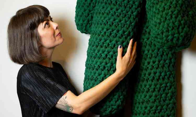 Artista Daniela Schneider abraa escultura feita de croch na cor verde
