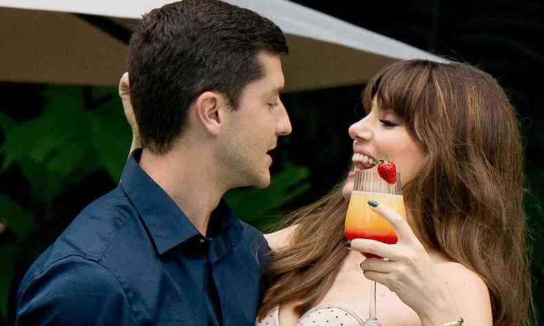 Ator Klebber Toledo abraa a atriz Camila Queiroz, que segura copo de drinque com morango na borda, em cena do filme Procura-se