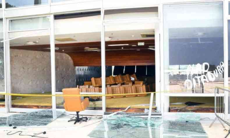 Fachada de vidro do STF quebrada e cadeiras de couro amontoadas dentro de uma sala. Em um vidro que no foi quebrado se l 'No ditadura'