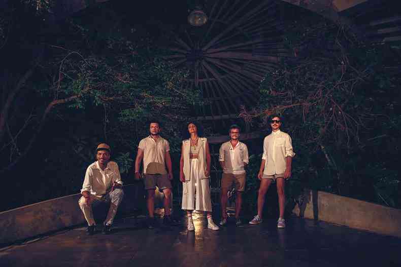 Os cinco integrantes do Graveola vestidos em tons de branco e cqui, em palco de teatro de arena 