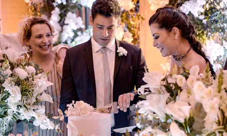 Em cena da novela ''Um lugar ao sol'', o ator Cau Reymond, com flor na lapela, parte bolo de casamento ao lado da sorridente personagem de Alinne Moraes