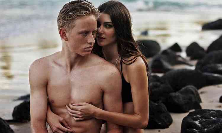 casal abraado em uma praia, ao entardecer