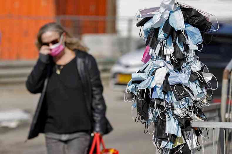 Mulher passa por poste com centenas de mscaras descartadas em Israel