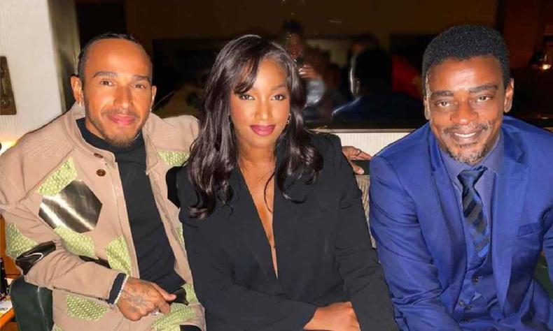 Iza posta foto de jantar com Lewis Hamilton e Seu Jorge e viraliza nas redes(foto: Reprodução/Instagram) Lewis Hamilton, usando jaqueta marrom claro e blusa preta, Iza, usando blazer preto e Seu Jorge Usando terno, camisa e gravatas azuis em restaurante