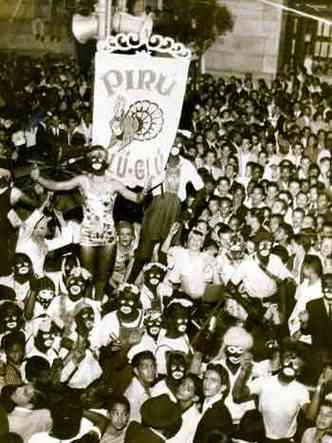Foliões reunidos na Rua Goiás, em BH, levam estandarte onde está desenhado um peru, no carnaval de 1950. Vários têm o rosto pintado de preto
