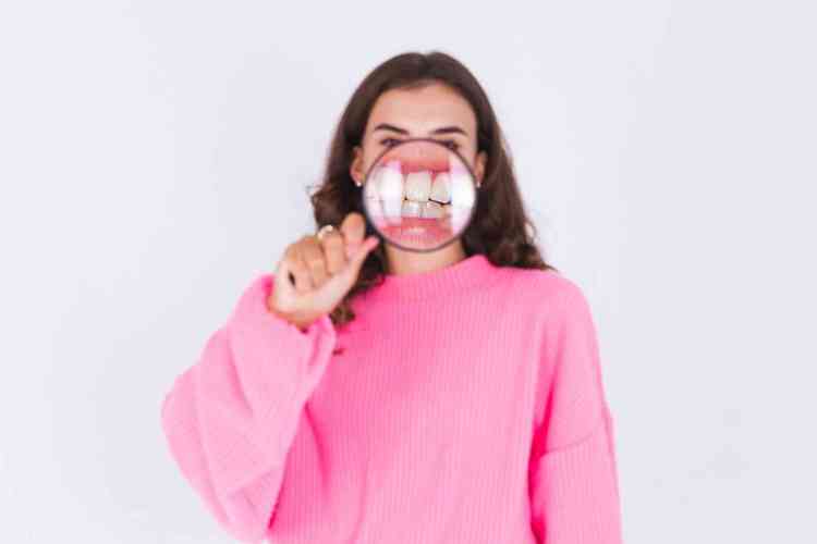Mulher de moletom rosa segurando uma pula a frente da boca mostrando os dentes