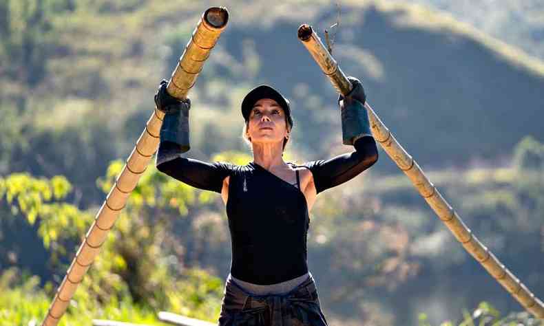Usando bon, atriz Danielle Winits olha para cima, tendo um bambu em cada mo. Ao fundo, v-se montanha e rea verde 