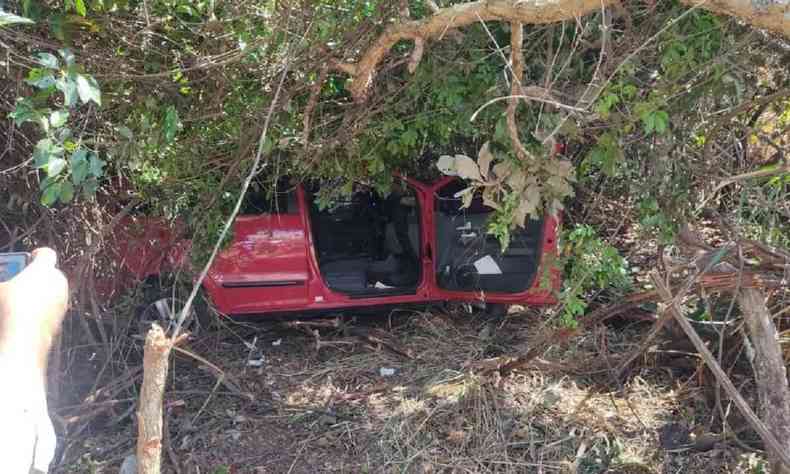 Carro vermelho acidentado no fim de um barranco sob rvores