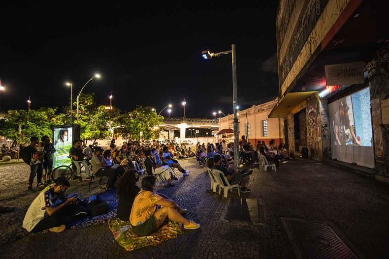 Pessoas sentadas no cho e em cadeiras assistem a filme exibido na fachada de teatro, em BH