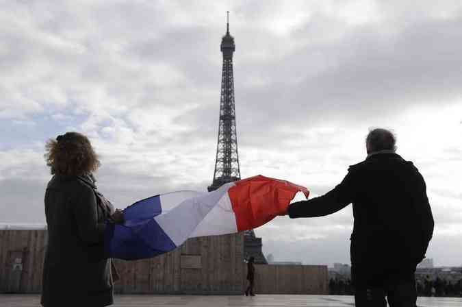 Casal segura a bandeira francesa em frente  Torre Eiffel durante o minuto de silncio