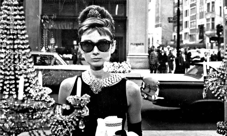 Atriz Audrey Hepburn, elegante e usando culos escuros, est em frente a uma vitrine em cena do filme Bonequinha de luxo 
