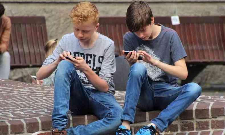 dois garotos sentados na calada no conversam, s tm ateno para o celular em mos