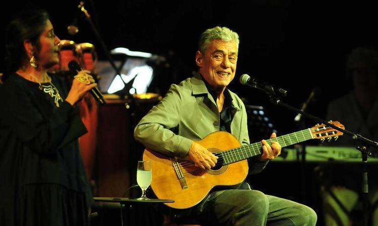 Chico Buarque sentado em um banco durante show