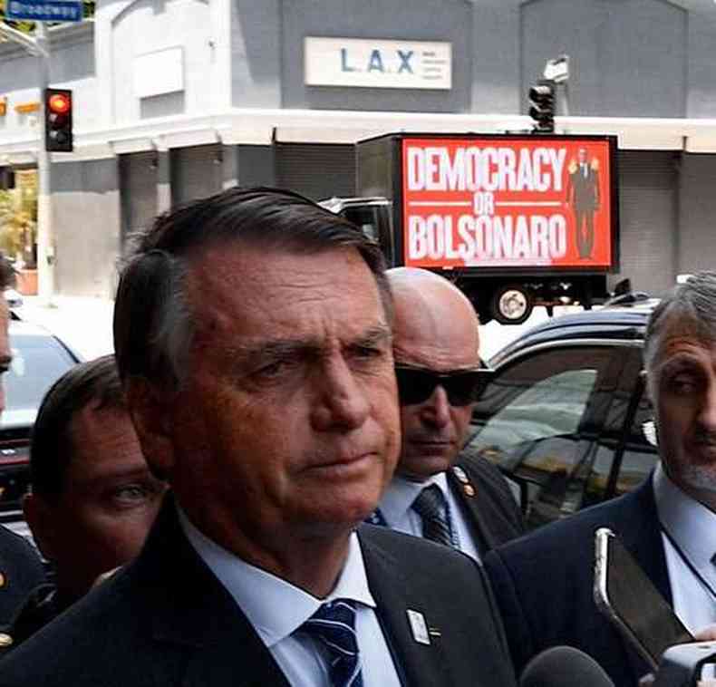 Bolsonaro em primeiro plano com automvel com crticas a ele ao fundo